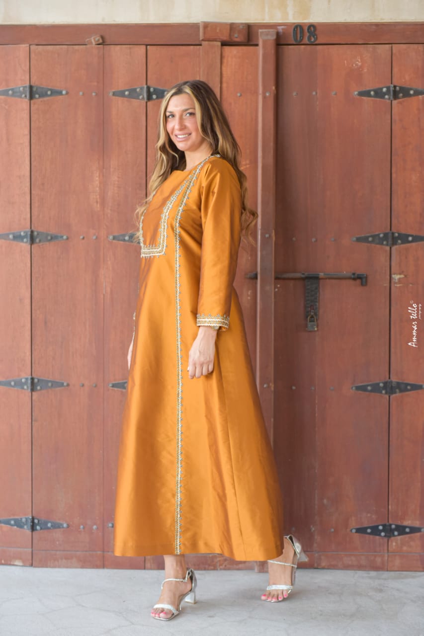 فستان برونزي فضفاض ذو طابع عربي مميز، قصة مستقيمة مزين بكشكشة وشرائط مصنوعة يدوياً