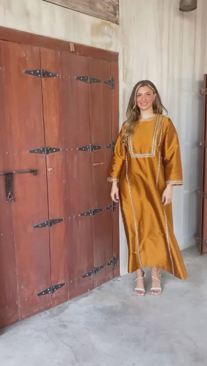 فستان برونزي فضفاض ذو طابع عربي مميز، قصة مستقيمة مزين بكشكشة وشرائط مصنوعة يدوياً